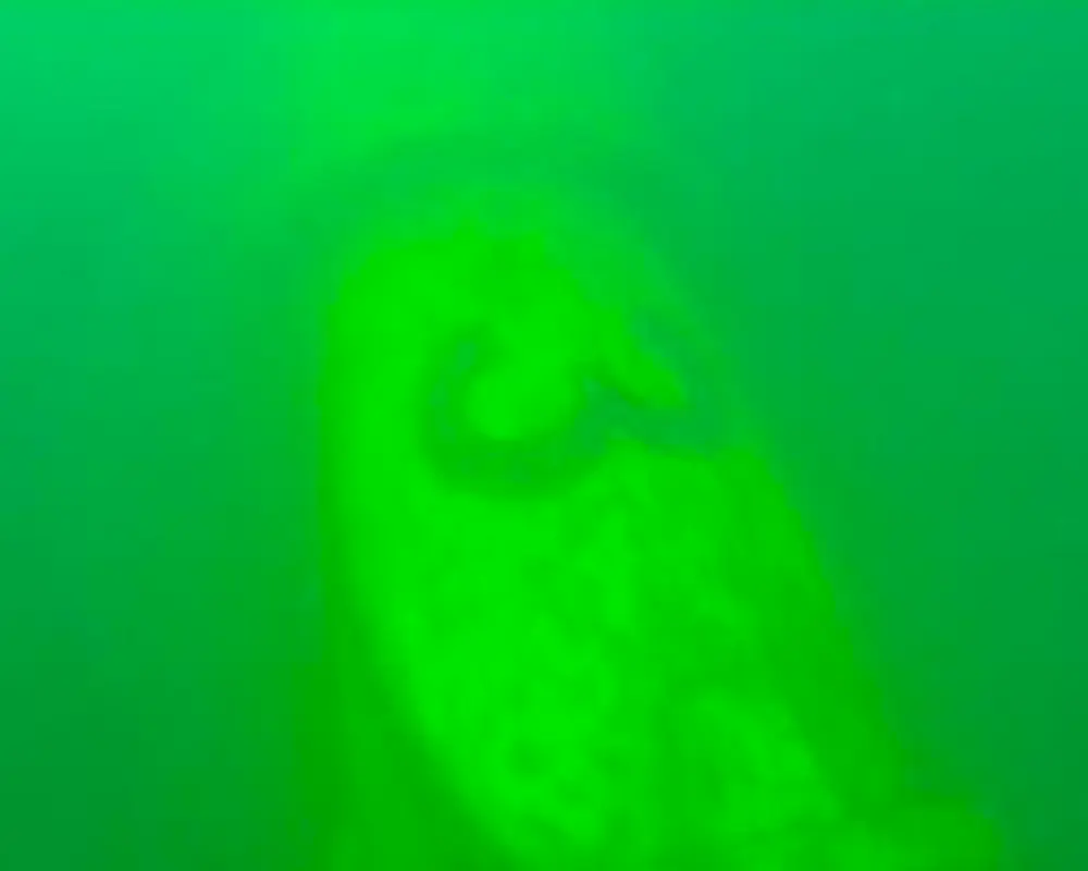 An underwater pipe seen through a camera in turquoise water. The number 3 is barely visible on the pipe.